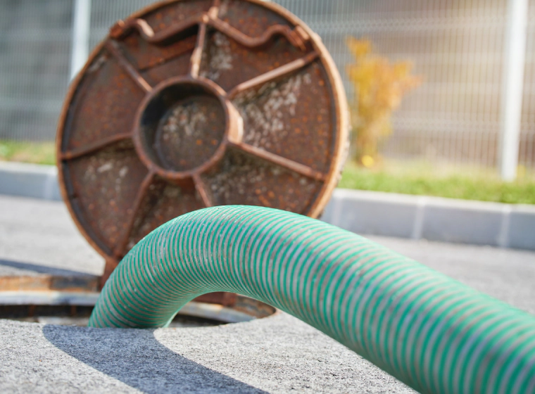 sewer line with a brown iron cover and a green hose inside